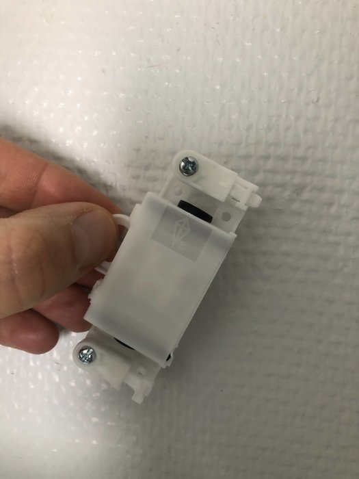 En hand håller en ip44 dubbelisolerad armatur mot en texturerad vägg.