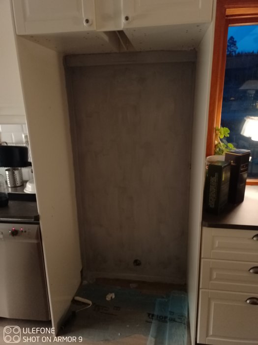 Köksrenovering med vägg som är förberedd för målning, skyddad golvdel och köksskåp.