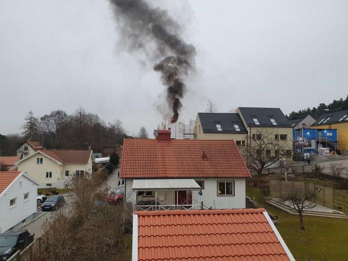 Mörk rök stiger från en byggarbetsplats bakom bostadshus, tecken på en brand i utveckling.