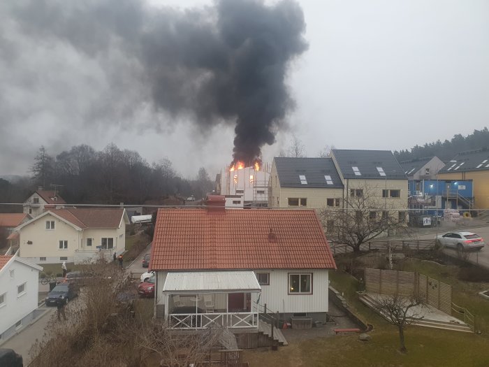 Brand i byggstomme av cellplastblock med betong, tjock svart rök stiger upp över hus.