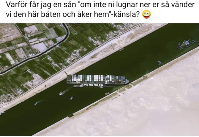 Flygbild på ett stort containerfartyg märkt "EVERGREEN" som är fast vid kanalkanten med bogserbåtar runt omkring.