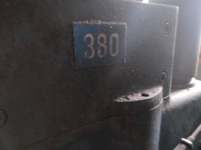 Närbild av ett mörkt metallföremål med numret 380, skruvhål synliga för demontering.