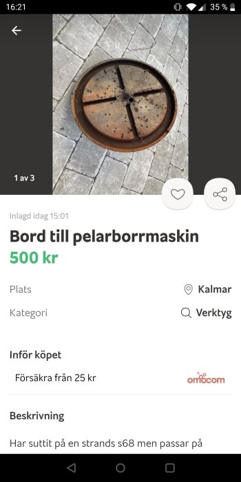 Rostig metallskiva som är en del av en pelarborrmaskin, ligger på ett stenbelagt underlag.