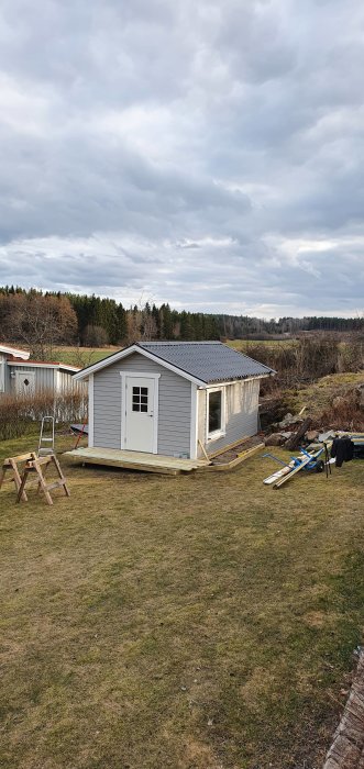 Nybyggd stuga med grått plåttak och påbörjade altankonstruktioner på en gräsmatta.