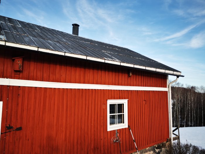 Rött stall med svart tak och loft som potentiellt hemmakontor.