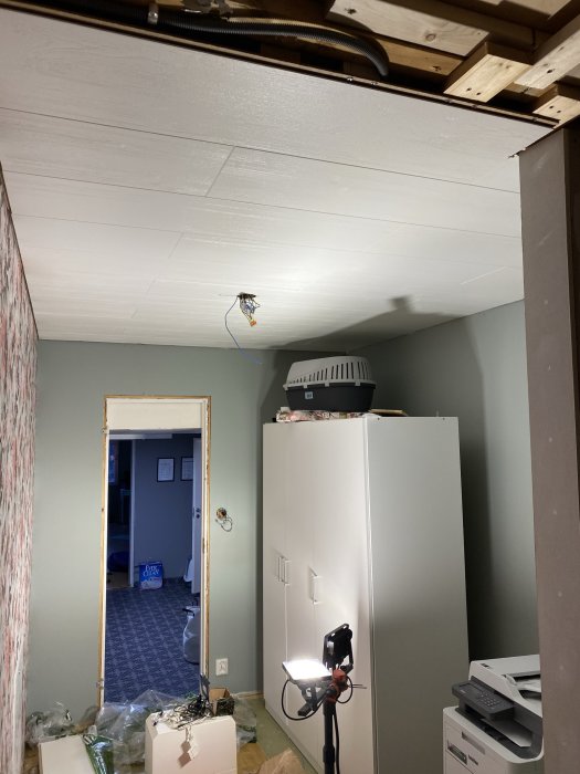 Renovering i hemmiljö med nyinstallerat vitt tak och tillfällig belysning, oordning på golvet.