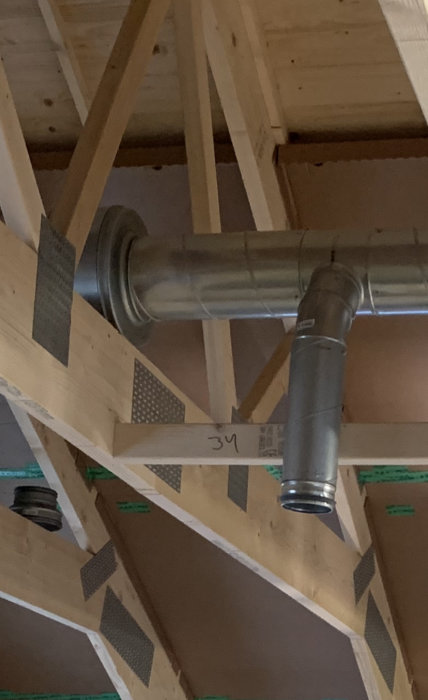 Ventilationsrör och ljuddämpare monterade mellan träbjälkar i ett tak under konstruktion.