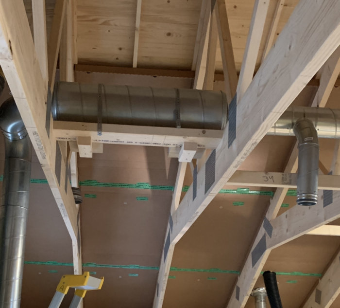 Ventilationsrör och ljuddämpare monterade mellan träbjälkar i ett pågående byggprojekt.