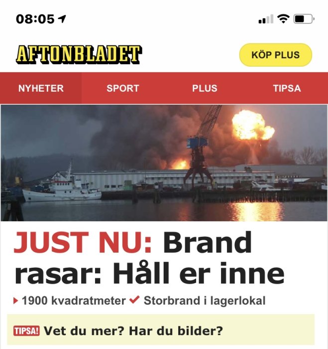 Skärmbild av nyhetsartikel med bild på stor brand på hamnområde, rök och lågor synliga.