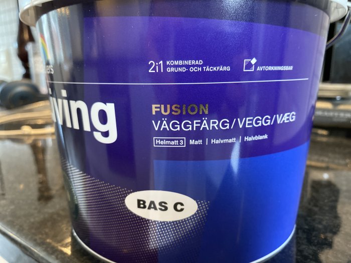 Burk med väggfärg märkt "Fusion" och texten "2 i 1 kombinerad grund- och täckfärg".