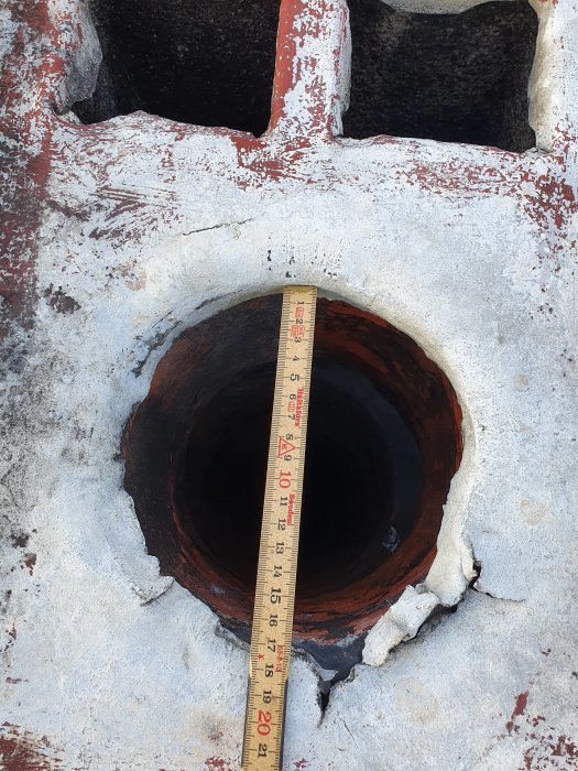 Mätsticka lutar mot en öppen skorsten för att mäta dess diameter, synlig förfall och rost runtom.