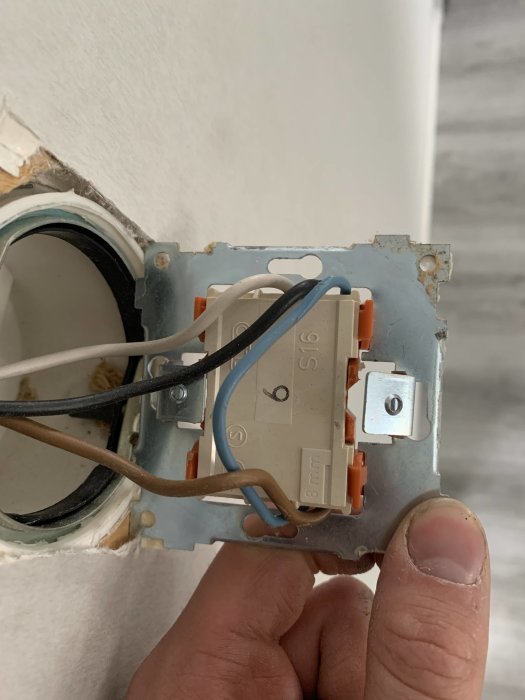 Elektrisk vägguttag utan kopplingsschema med synliga trådar och terminaler, hand håller i det.