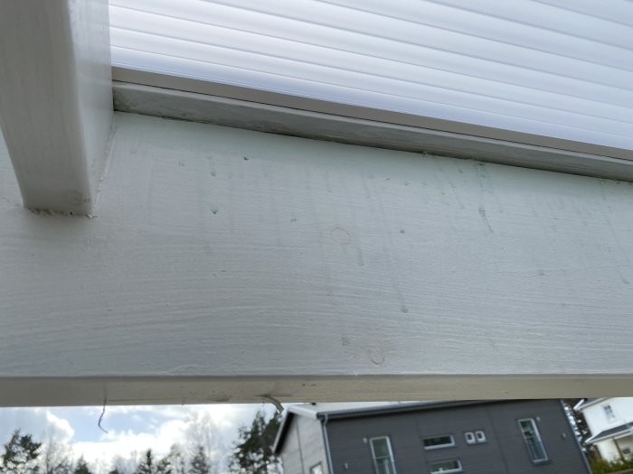 Vitmålat trä på altantak med gröna fläckar och avfärgning, möjliga tecken på fukt eller felaktig målning.
