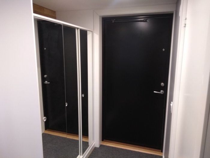 Hall i Attefallshus med begagnad garderob och svart ytterdörr, inklädd med Ikea täckskiva.