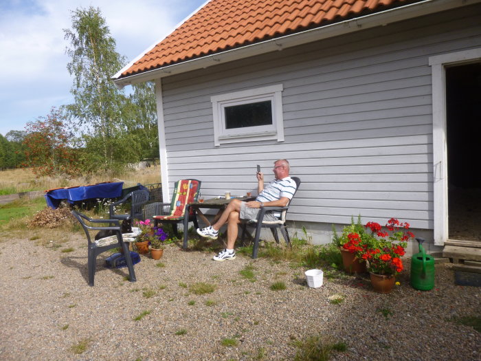 Hus med liggande dubbelfas-panel och person som sitter på stol och använder mobiltelefon.