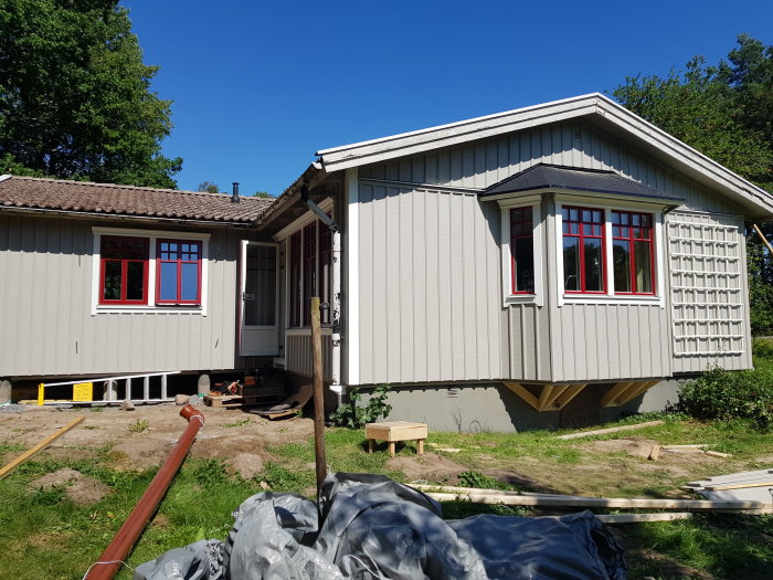 Ett nyligen renoverat hus med röda fönsterkarmar och avlägsnad ställning, i soligt väder.