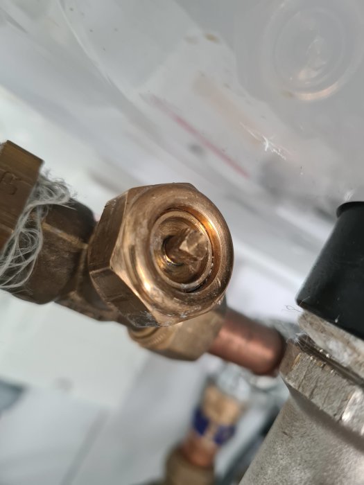 Närbild på en avluftningsventil i mässing som läcker vatten, monterad på ett rörsystem.