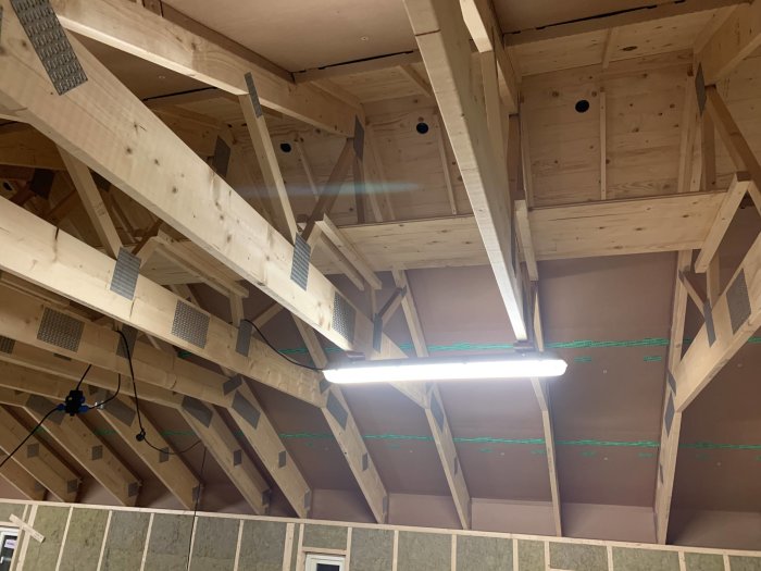 Takstolar och isolering i ett pågående övervåningsbygge med synliga träbjälkar och glespanel.