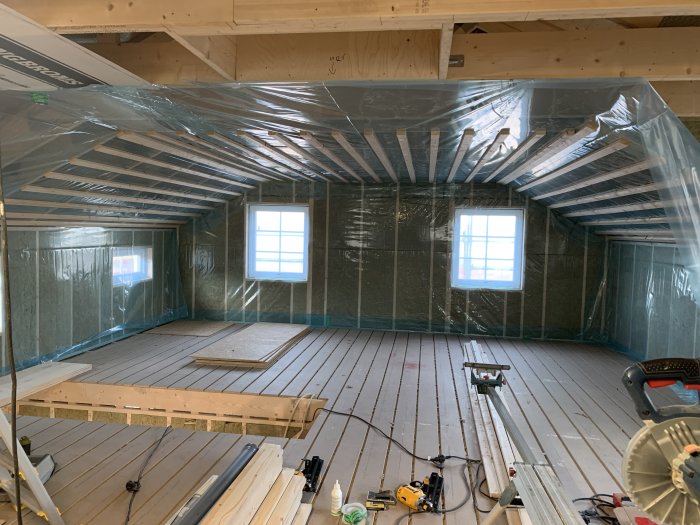 Interiör av ett renoveringsprojekt i ett vindrum med isolering och verktyg.