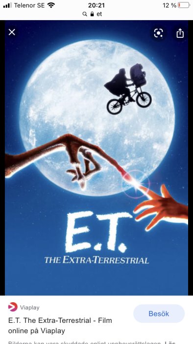 Silhuett av en pojke och E.T. på en cykel mot månen, fingertoppar nästan rör vid varandra.