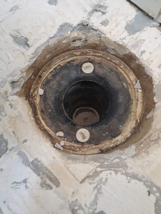 En gammal svart golvbrunn i ett badrum med synbara rester av flytspackel och betong runtomkring.