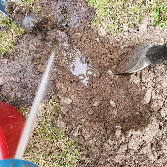 Vatten hälls på en jordhög bredvid en spade, i arbetet med att sprida jord på marken.