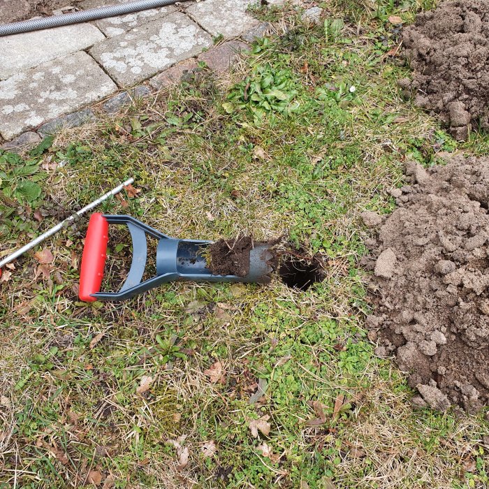 Plantskopa med jord i gräsmattan bredvid en hög med grävd jord.