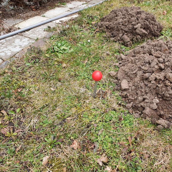 Jordhögar på en gräsmatta med en röd plastboll ovanpå ett metallrör i förgrunden.