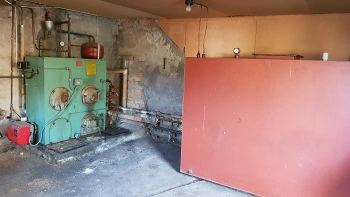 Ett gammalt utrymme med en grön oljepanna, röda och vita väggar, samt synligt slitage och tomma ytor.
