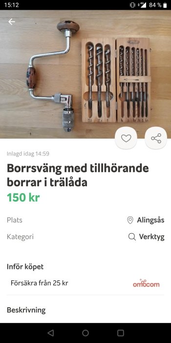 Gammaldags handborrsväng av metall tillsammans med träetui fyllt med borr i olika storlekar.