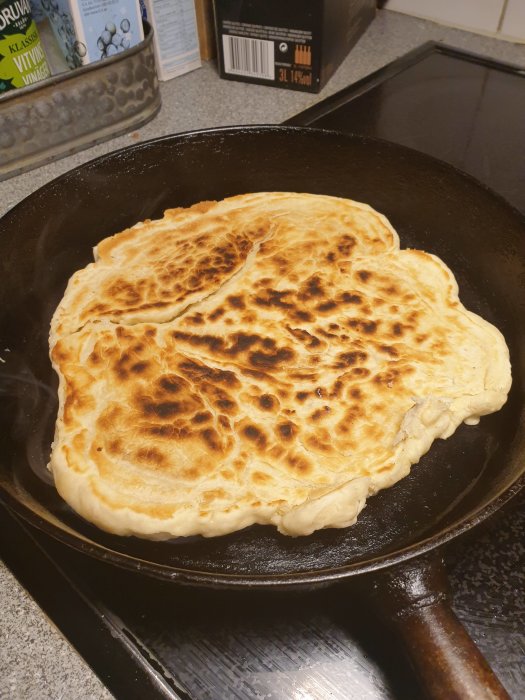 En stor, gyllenbrun pannkaka som gräddas i en gjutjärnspanna på en spis.