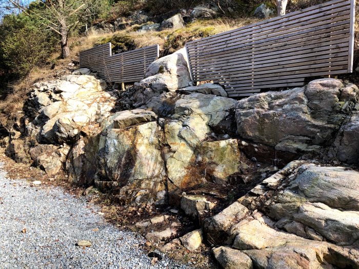 Naturligt klippigt bergslandskap på baksidan av ett hus med texturrika stenar och lite vegetation.