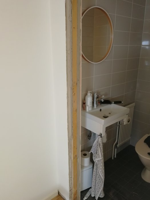 Renoveringsarbete i badrum med borttagen väggsektion nära handfat och spegel.