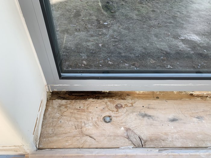 Vattenskada och röta på träsyll under ett fönster från golv till tak, med felmonterat fönsterbleck.