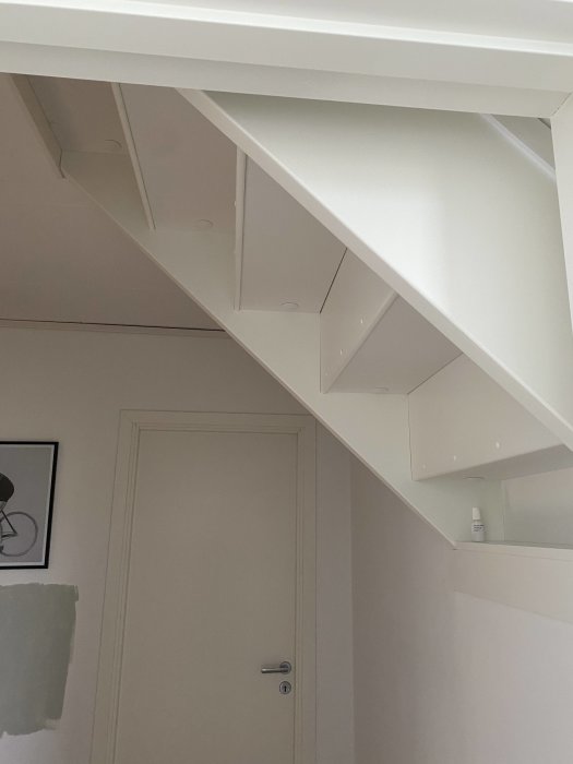 Vit trappa i en hall som går in i en vägg, isolerad underifrån med enkla träskivor synliga.