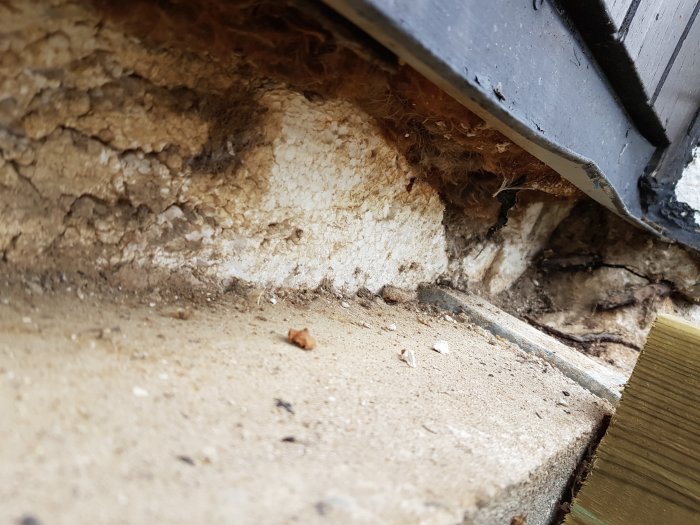 Skadad isolering och sten vid en husgrund där en gammal stentrappa avlägsnats, risk för gnagare.