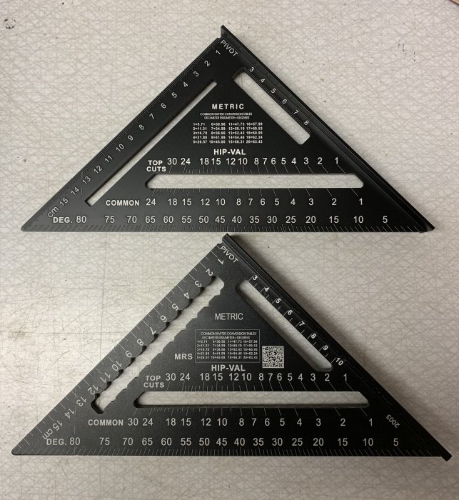 Två svarta snickarvinklar med vit märkning för tum och metriska mått placerade ovanpå varandra på en arbetsyta.