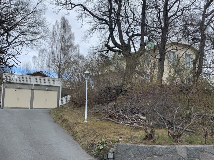 Bild av ett garage med betongvägg framför äldre trähus, med omgivande grönska och en infartsväg.