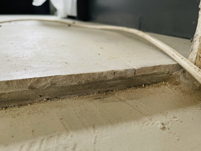 Närbild av mörka fogar på betonggolv med potentiell fuktskada och elektrisk kabel på ytan.