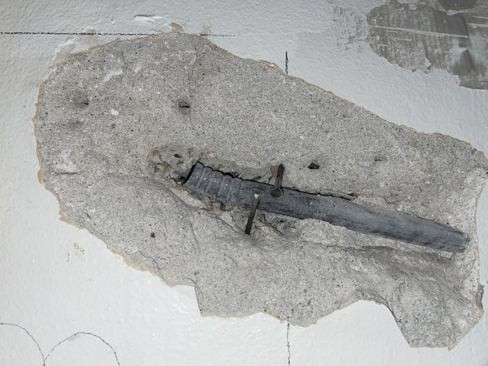 Skadad vägg med ett avlagrat lager puts som avslöjar underliggande träull och armatur.