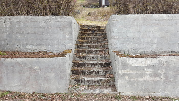 En äldre betongstödmur från 1978 med synliga sprickor och en mellersta trappa som visar tecken på slitage och lutning.