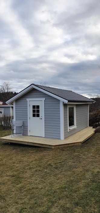 Nyligen färdigställd trädäck runt litet grått hus med vita knutar och ett svart tak.