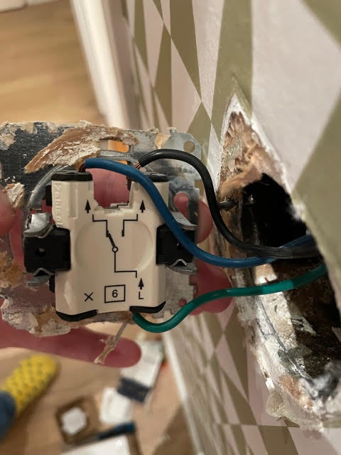 Elektrisk dosa med slumpmässigt kopplade blå och grön-gula ledningar, synliga i en vägg.