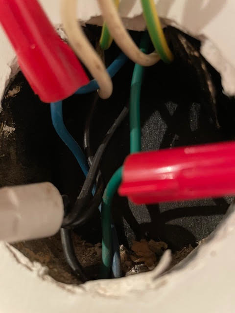 Eluttag med trånga elektriska kopplingar inklusive blå och vit ledning samt jordtråd i en vägg från 60-talet.