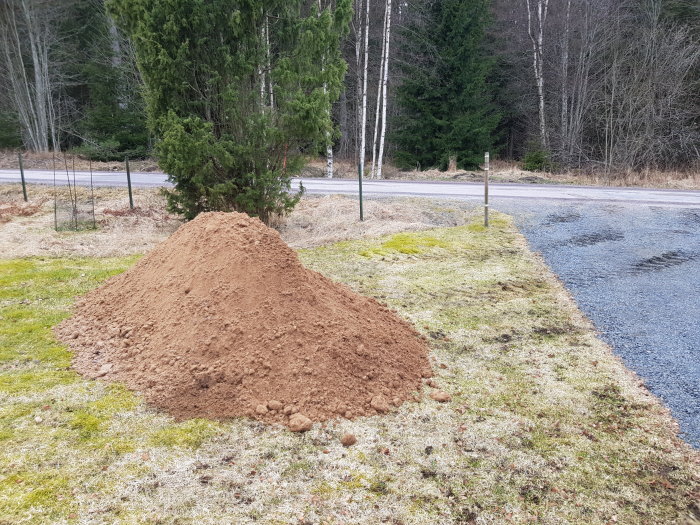 Hög med sand levererad på en gräsmatta för användning i barns sandlåda, med träd i bakgrunden.