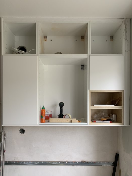 Omonterade vita väggskåp i ett kök med en synlig ojämnhet mellan skåpen och taket.