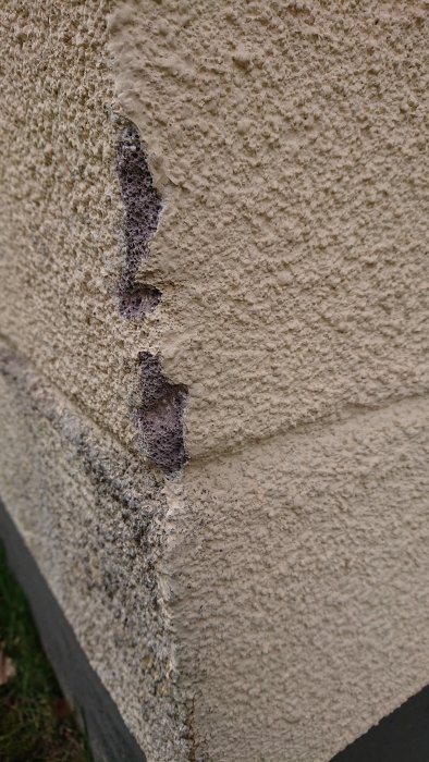 Skadad fasad där underliggande lager likt blåbetong blottas.