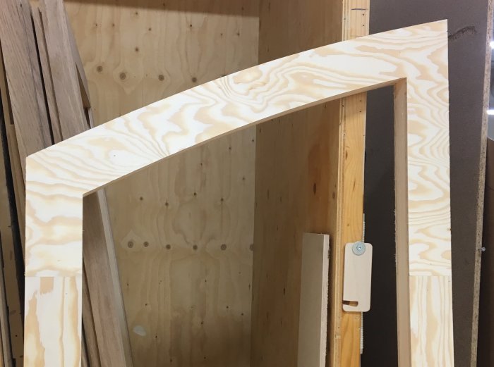 Trämall i form av en böjd plywoodbit som skall användas för att mäta och avbilda en dörröverstycke.