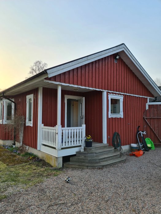 Röd stuga med vit entrétrappa och räcke. Trappan verkar gammal och potentiellt ruttet.
