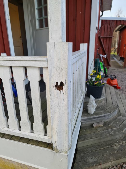 Skadad och rötskadad trästolpe på en entretrappa med synlig förfall och flagnande vit färg bredvid en dörr.
